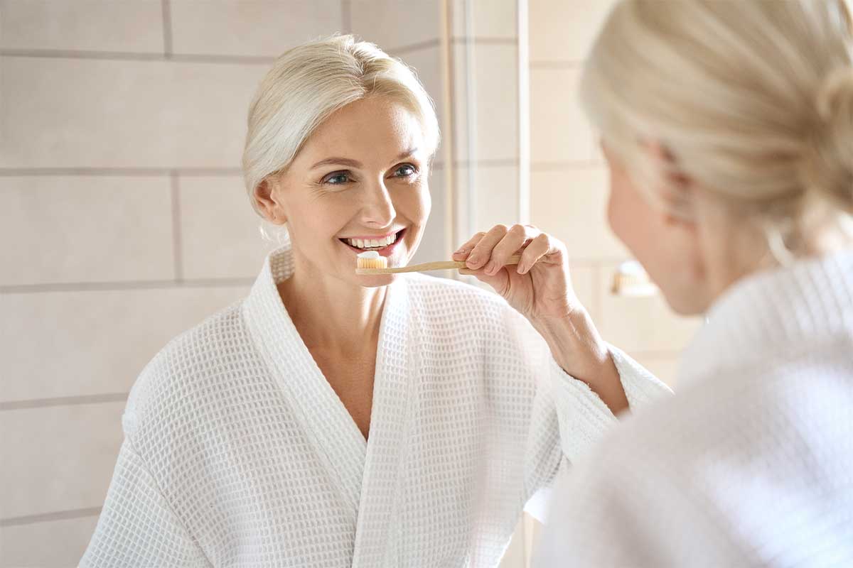 long-term-cost-savings-dental-implants-smile women smiling about implant cost savings while brushing her new dental implants